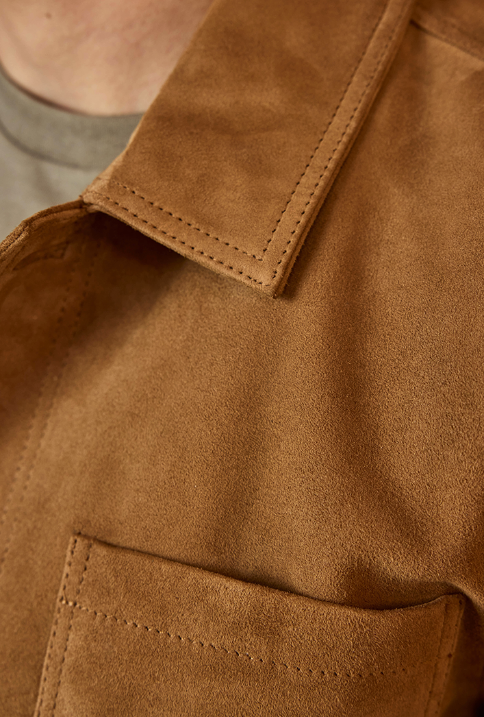 Close-up of a brown tan suede jacket with a pocket and collar.